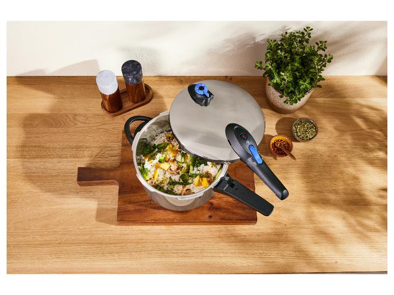 Een snelkookpan met rijst en groenten, kruiden en een plant op een houten tafel.