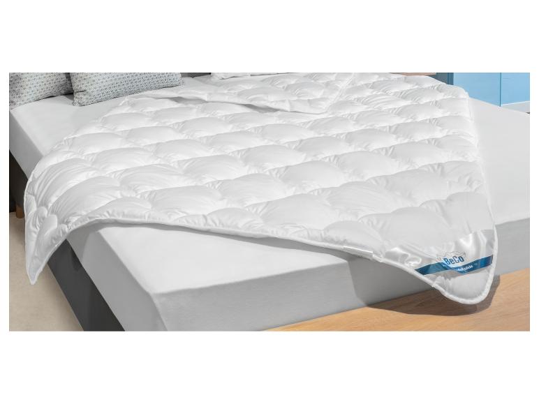 Wit gewatteerd dekbed op een bed met een wit laken en kussens met geometrisch patroon.