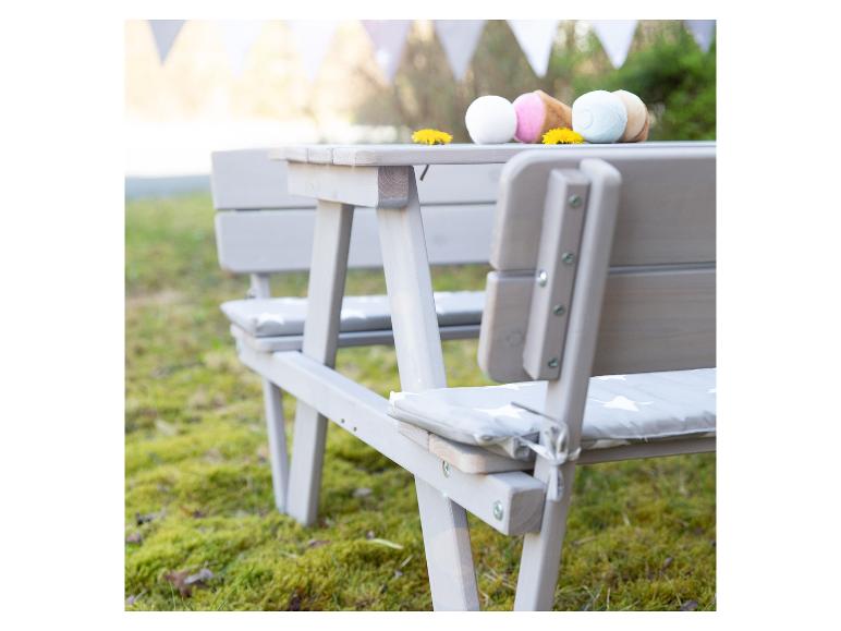 Grijze picknicktafel met banken en kussens, versierd met speelgoedijsjes en paardenbloemen.