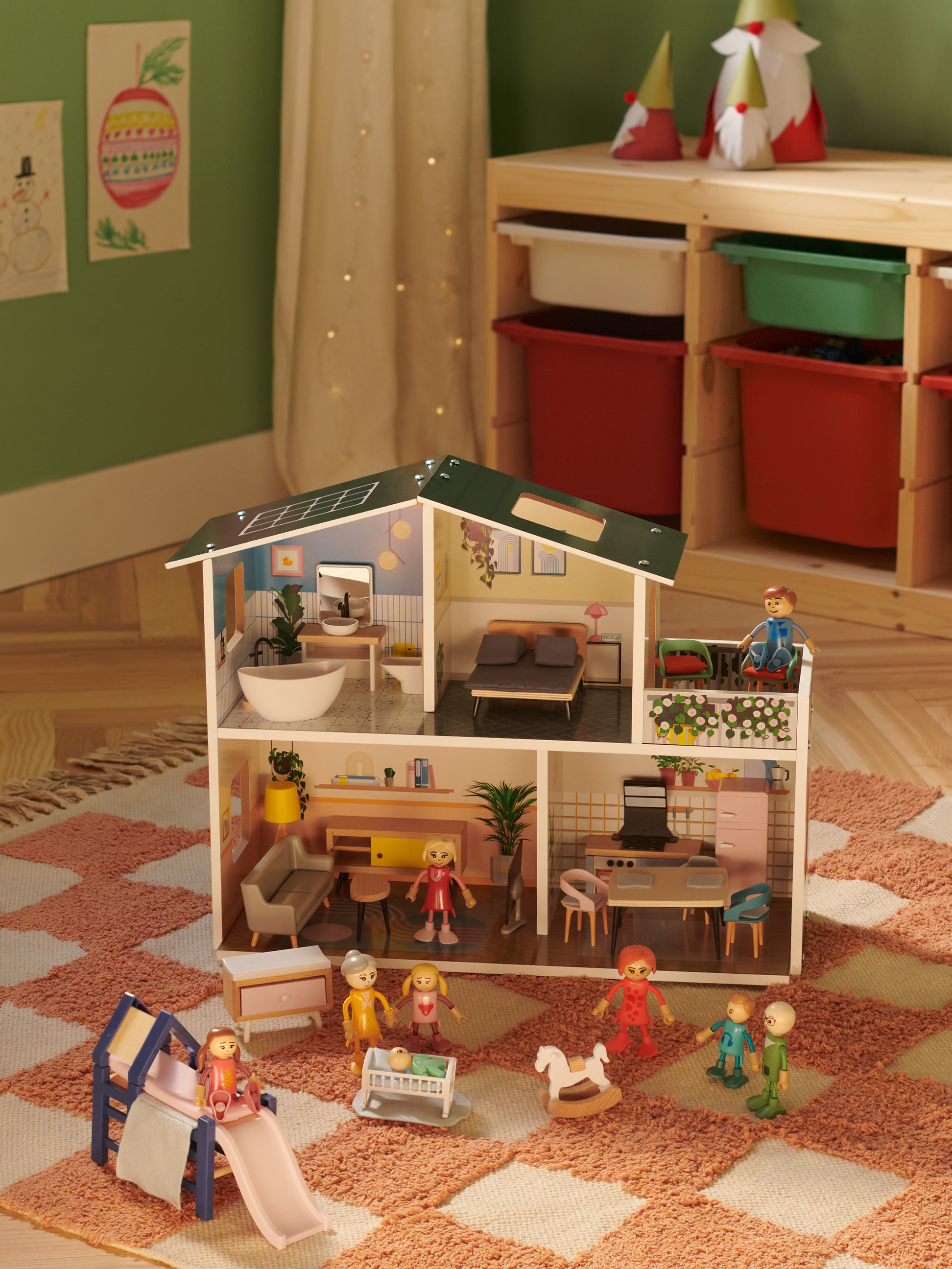 Houten poppenhuis met figuren en meubels, omringd door een vloerkleed en speelgoed.