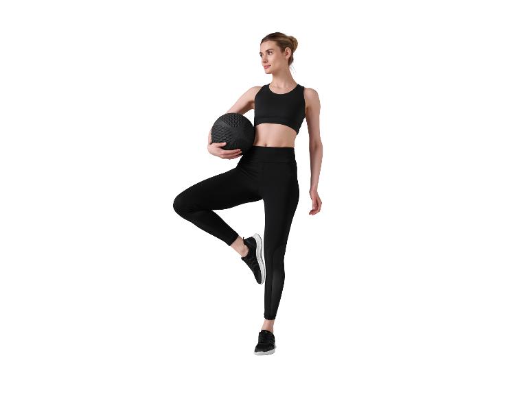 Vrouw in zwarte sportkleding met een medicijnbal, balancerend op één been.