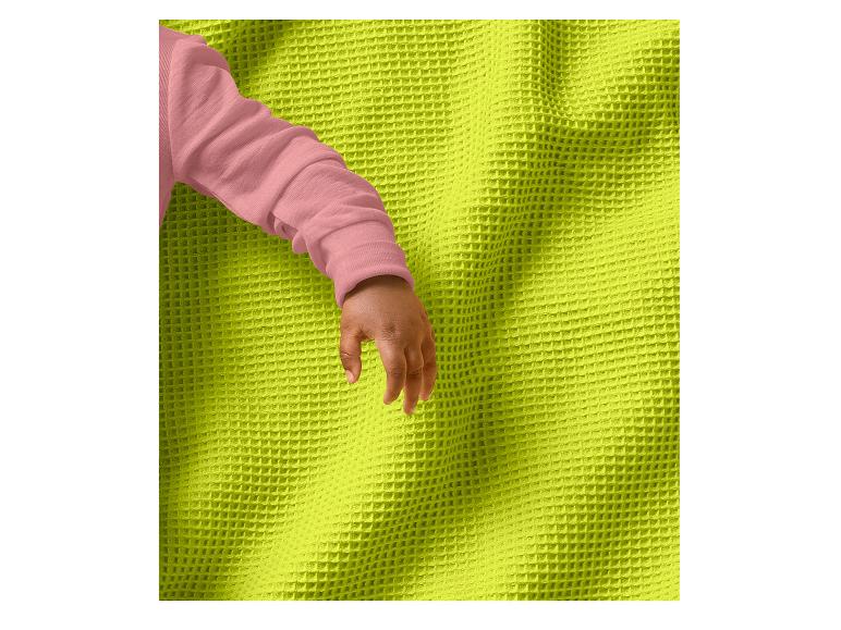 Babyhandje met roze mouw op een limoengroene wafel deken