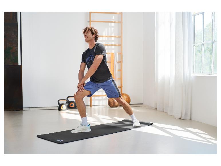 Man rekt op een fitnessmat, draagt een sportshirt en korte broek.