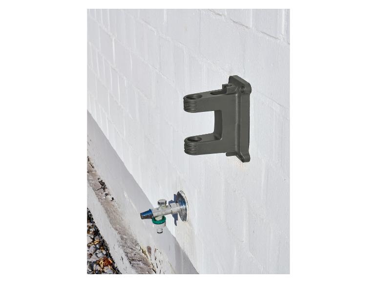 Donkergrijze muurbeugel en waterkraan met slangconnector op een witte bakstenen muur.