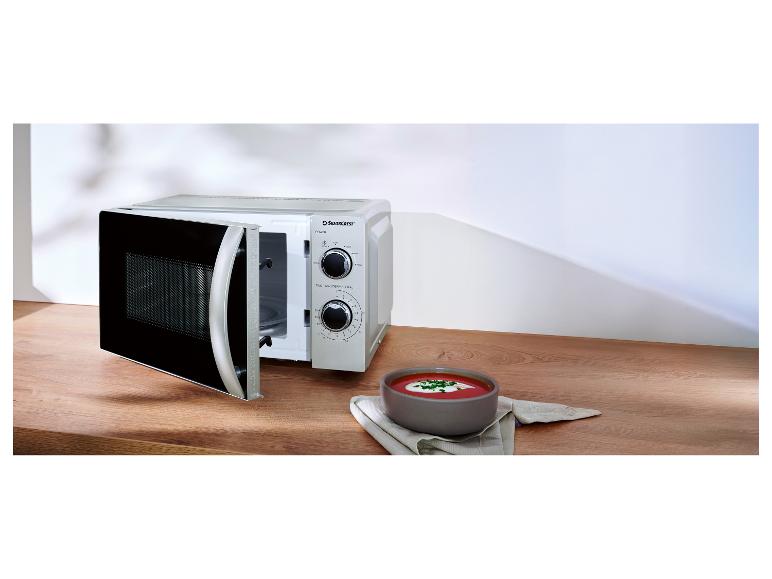 Silvercrest magnetron met open deur en een kom soep op een houten tafel.