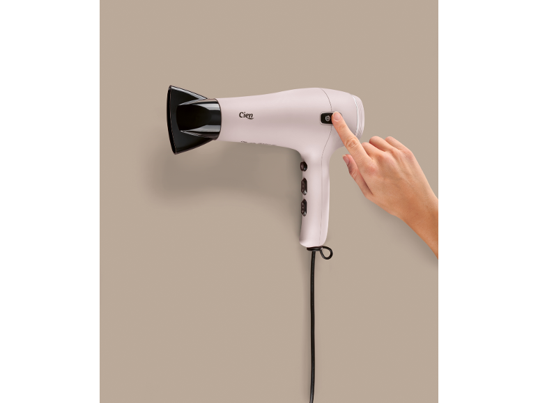 Roze föhn met zwart mondstuk, een hand drukt op de aan/uit-knop.