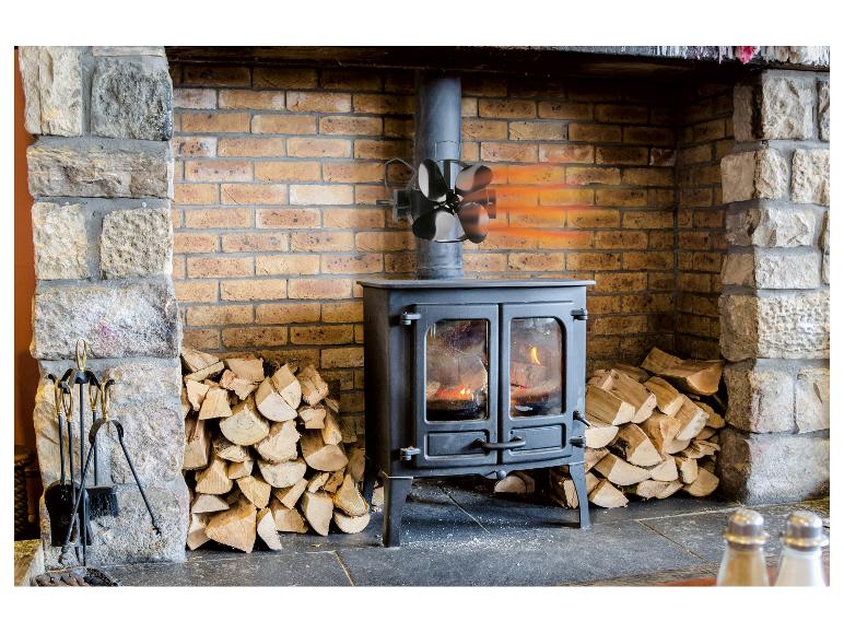 Houtkachel met warmteventilator en houtstapels in een stenen en bakstenen open haard.