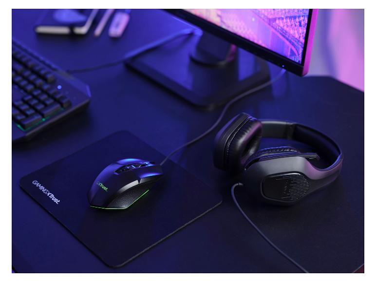 Gamingmuis en koptelefoon op een muismat, naast een toetsenbord en monitor.