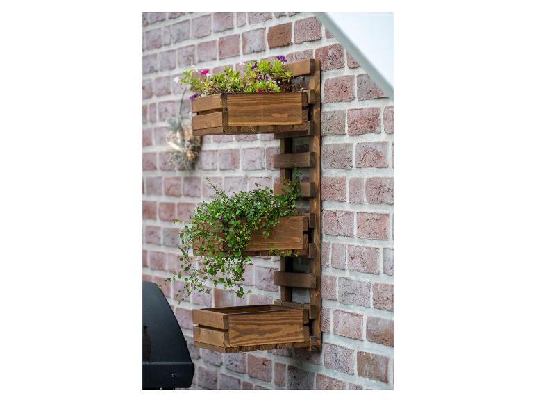 Houten verticale wandtuin met bloemen en groen aan een bakstenen muur.