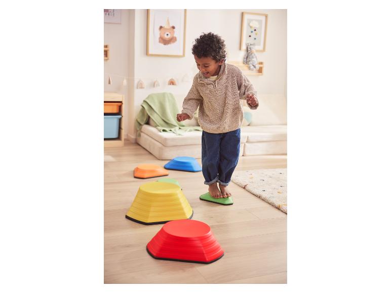 Blij kind speelt met kleurrijke stapstenen op een houten vloer.