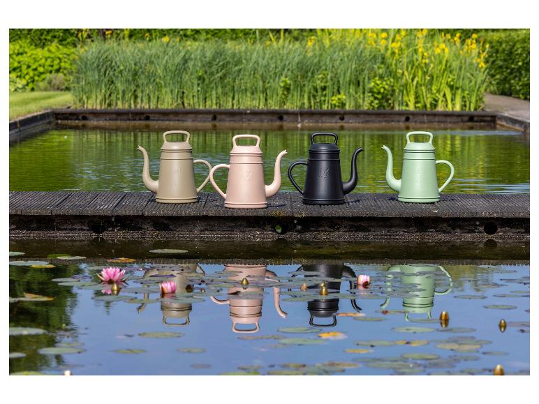 Vier gieters in verschillende kleuren op een vlonder bij een vijver, met reflecties in het water.