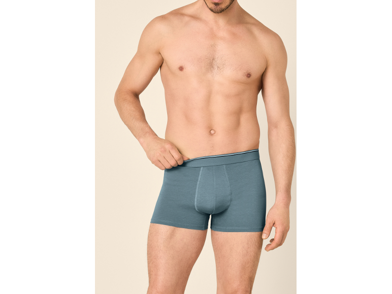 Man poseert in grijze boxershorts met blauwe tailleband.