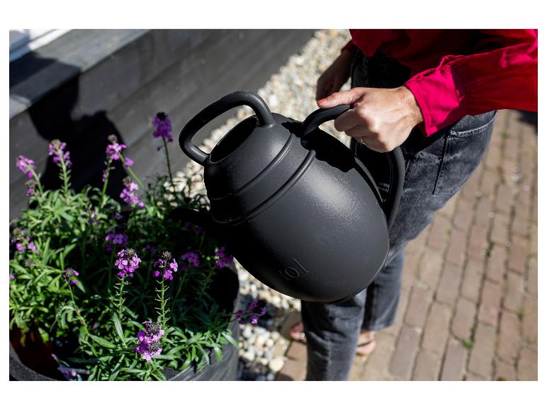 Persoon giet paarse bloemen water met een zwarte gieter.