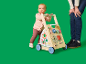 Baby speelt met een houten activiteitenloopwagen, met een volwassene ernaast.