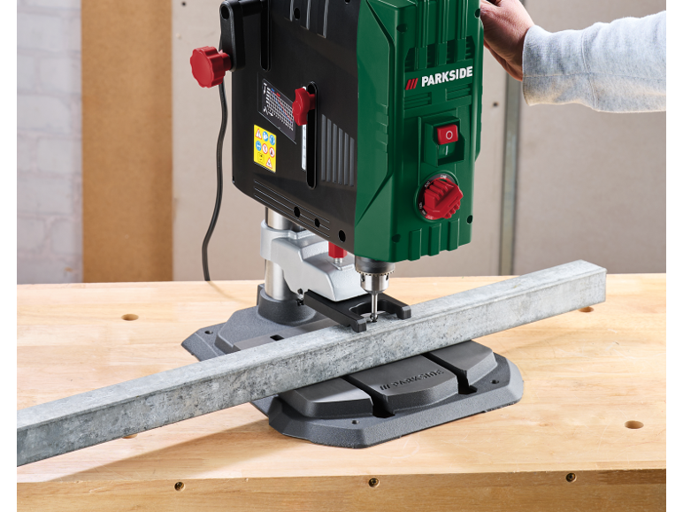 Tafelboormachine boort in een metalen profiel op een houten werkbank.