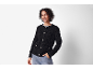 Lachende vrouw in een zwart getextureerd vest en jeans, hand in zak.