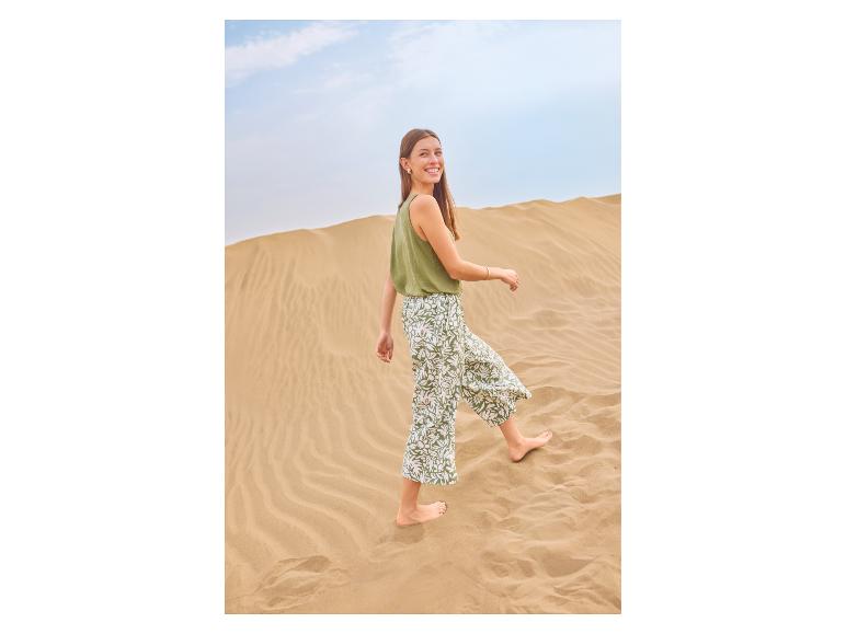 Vrouw in groene top en bedrukte broek loopt blootsvoets door zandduinen.