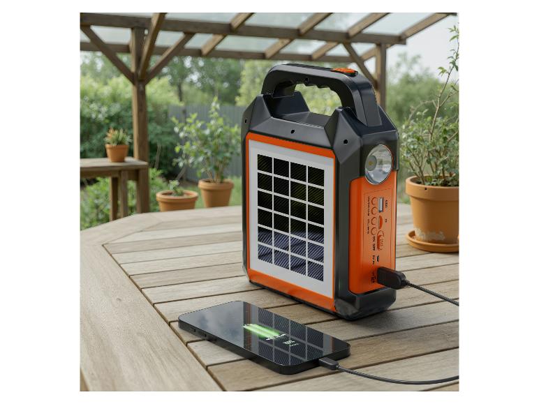 Zwart-oranje draagbare zonnelader met een opladende telefoon op een houten tafel.