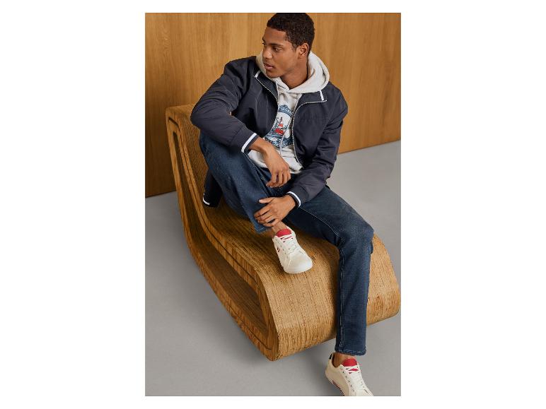 Man in ESMARA MEN hoodie, blauwe jas en jeans op een houten bank.