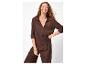 Vrouw in bruine blouse en broek, met gouden sieraden, lachend.