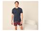 Man in een marineblauw T-shirt en rood geruite boxershort, lachend in een lichte kamer.