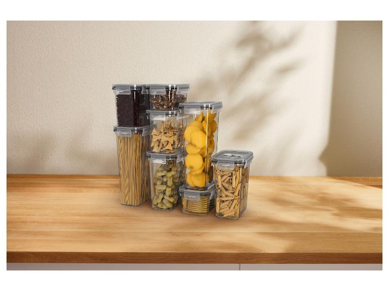Transparante voedselcontainers gevuld met pasta, noten en koffiebonen op een houten tafel.