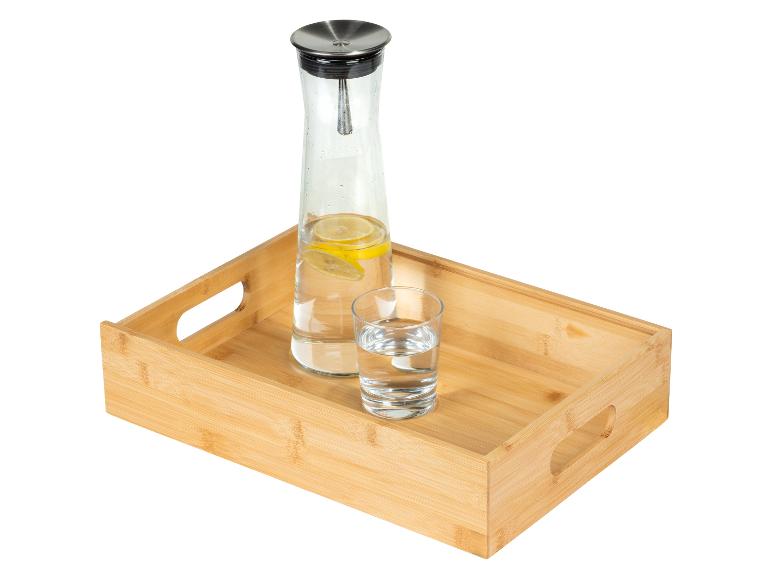 Karaf met citroenwater en glas op een bamboe dienblad.