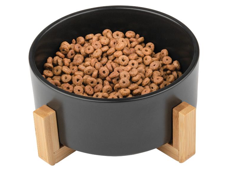 Een zwarte hondenvoerbak met houten standaard gevuld met hondenvoer.