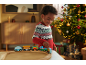 Lachend kind speelt met houten trein, verlichte kerstboom op de achtergrond.