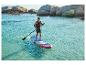 Man peddelt op een paddleboard in turquoise water met een rotsachtige kustlijn op de achtergrond.