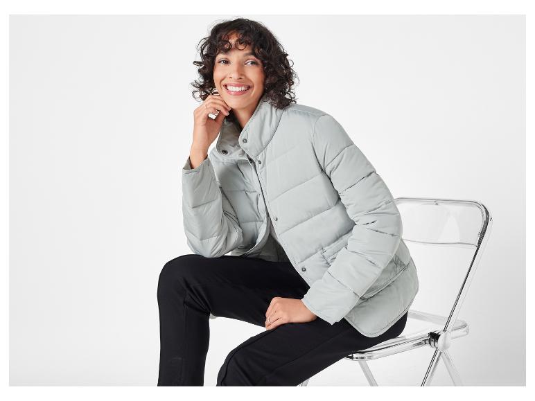 Een vrouw draagt ​​een lichtgrijze jas en zwarte broek.