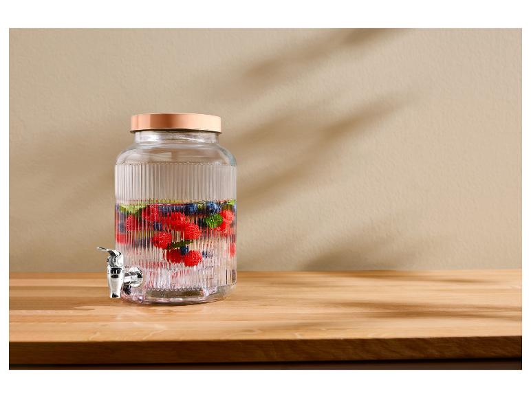 Glazen drankdispenser met bessen en munt op een houten tafel.