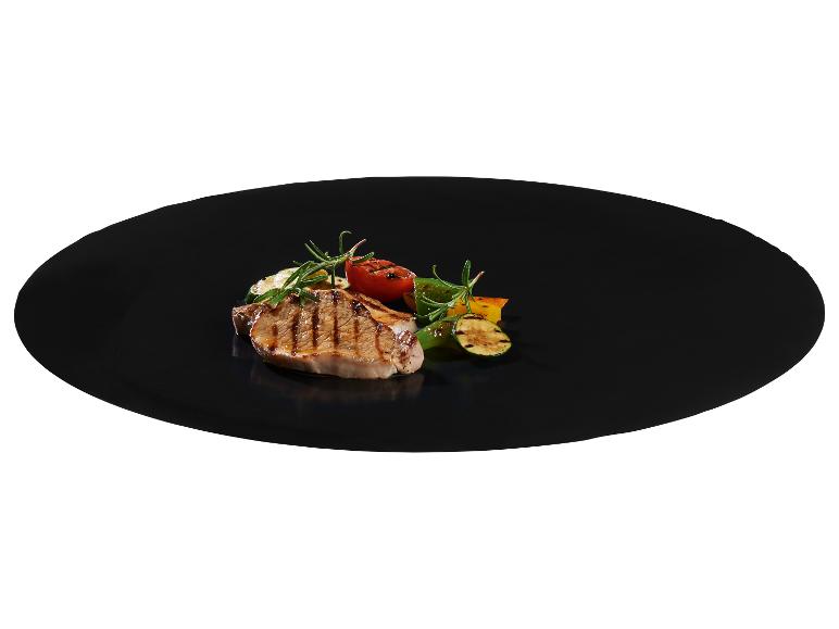 Gegrilde varkenskotelet met gegrilde groenten en rozemarijn op een zwart bord.