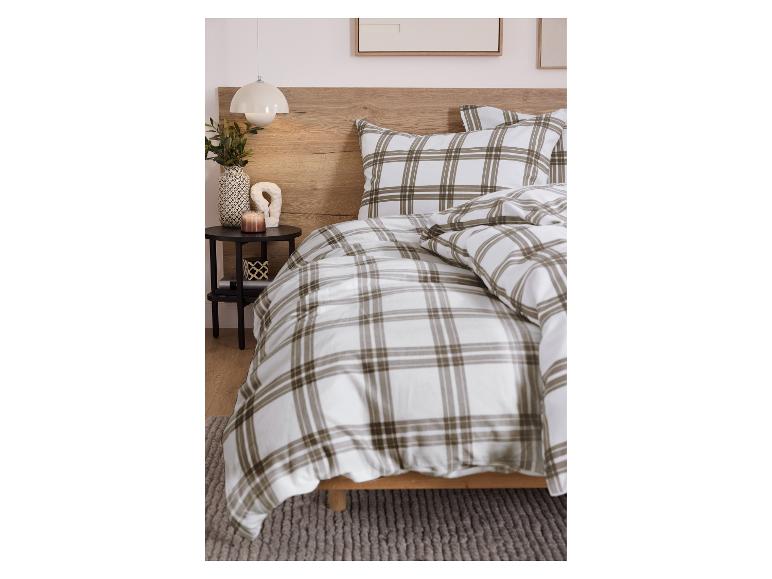 Slaapkamer met geruit beddengoed, houten hoofdbord en nachtkastje met decoraties.