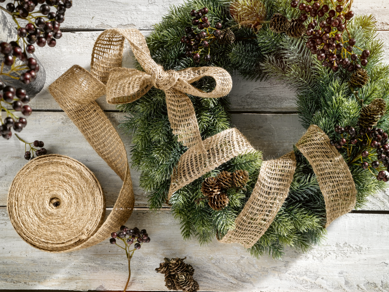 Kerstkrans met juten lint en bessen op een witte houten achtergrond.