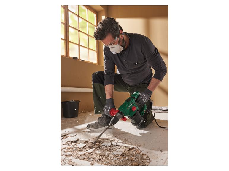 Een man met beschermende kleding gebruikt een Parkside sloophamer om tegels te verwijderen.