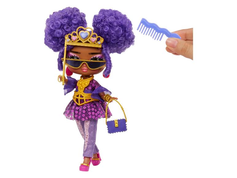 Een pop met paars haar, een gouden kroon, zonnebril en een blauwe tas.