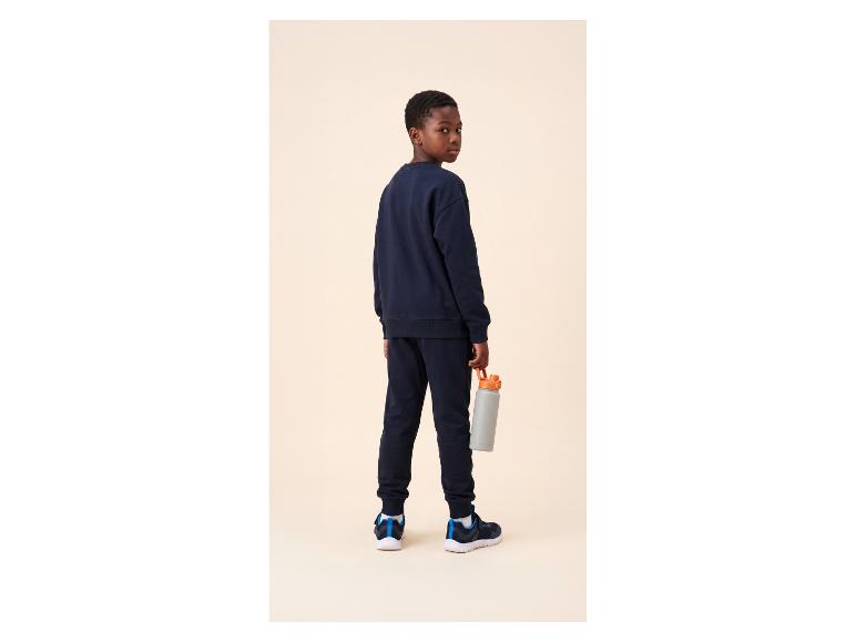 Jongen in een donkerblauw trainingspak en sportschoenen, met een grijze waterfles.