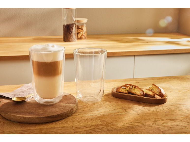 Latte in een dubbelwandig glas en biscotti op een houten tafel.
