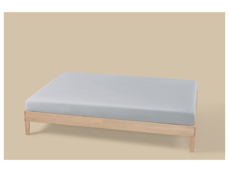 Bed met licht houten frame en grijs matras op een beige achtergrond.