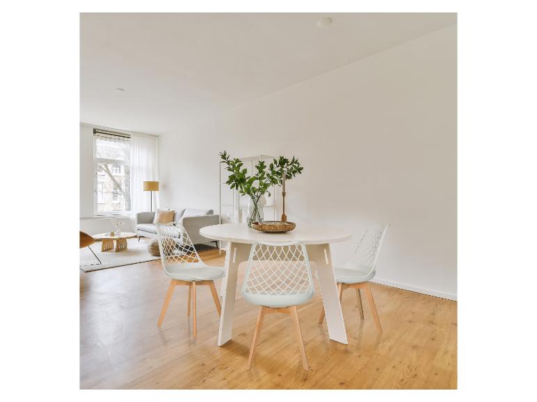 Lichte eet- en woonkamer met een witte ronde tafel, stoelen en een bank.