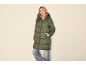 Vrouw in een lange, groene gewatteerde jas met capuchon en jeans.
