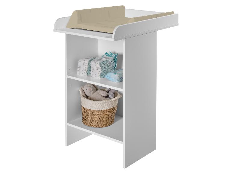 Witte commode met beige aankleedkussen, luiers en speelgoed in een mand.