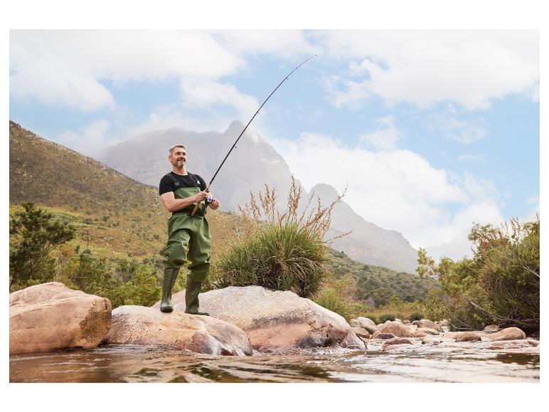 Man in viswaders en laarzen, met een vishengel bij een rivier.