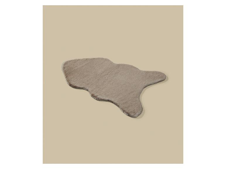 Een beige, onregelmatig gevormd imitatiebontkleed op een beige achtergrond.