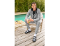 Man in grijs trainingspak en zwarte sandalen met witte sokken, lachend met een groene smoothie.