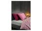 Bed met roze kussens en dekbedovertrek met geometrisch patroon, naast een nachtkastje met lamp.
