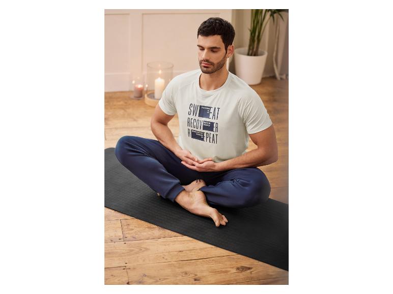 Man in een witte T-shirt met de tekst 'Sweat Recover Repeat' zit op een yogamat.