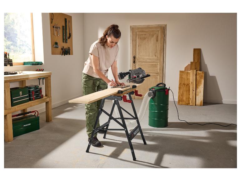 Vrouw gebruikt cirkelzaag en industriële stofzuiger om hout te zagen in een werkplaats.