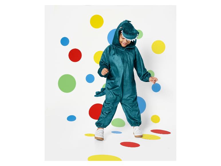 Een kind in een groene dinosaurus onesie loopt op gekleurde stippen.